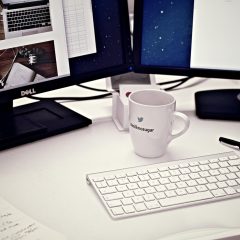 技术校对陈叙白在双屏工作站前核对汇率数据源与页面展示效果，屏幕上并排显示多个公开报价页面